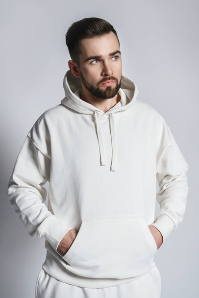 Handsome man wearing blank white hoodie and pants posing on gray background - Fotoğraf, Görsel