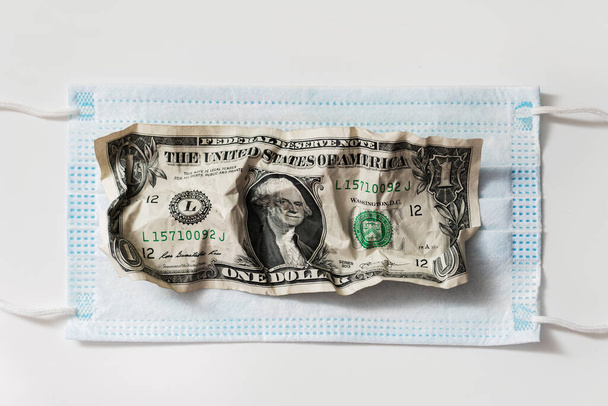 Closeup shot of crumpled one dollar bill on a disposable hygienic face mask. Concept of financial crisis after covid-19. - Foto, Bild