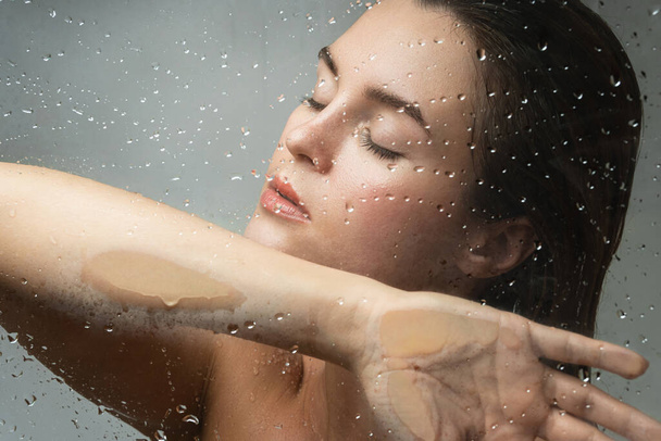 Portrait of beautiful and sensual woman captured through wet glass - Photo, Image