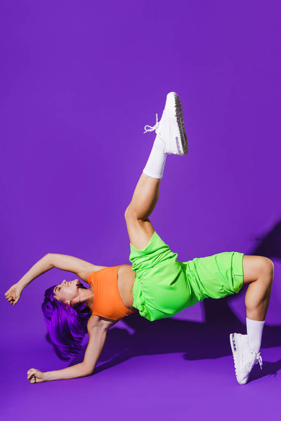 Carefree active woman dancer wearing colorful sportswear performing against purple background - Fotografie, Obrázek