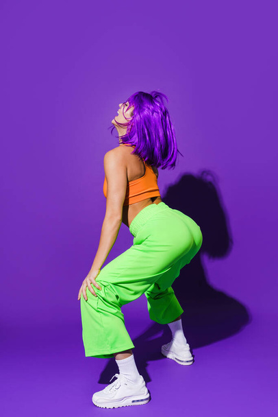 Carefree woman dancer wearing colorful sportswear twerking against purple background - Fotografie, Obrázek