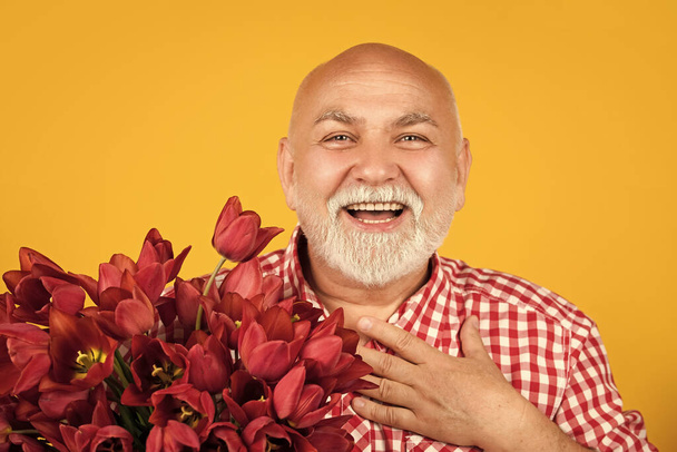 happy thankful old bearded man hold spring tulip flowers on yellow background. - Foto, Imagen