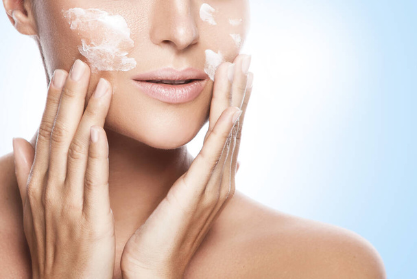 Young and beautiful woman applying moisturizing cream on her face - Photo, image