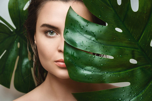 Portrait of beautiful young woman with a smooth skin holding Monstera deliciosa plant leaf - Valokuva, kuva