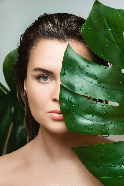 Portrait of beautiful young woman with a smooth skin holding Monstera deliciosa plant leaf - Fotó, kép