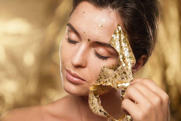 Beautiful young woman with golden shining mask on her face for skin treatment - Zdjęcie, obraz