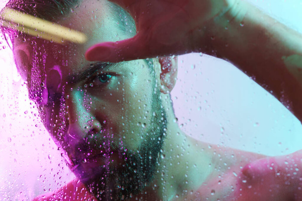 Portrait of handsome young man captured through wet glass in colorful neon light - Foto, Bild