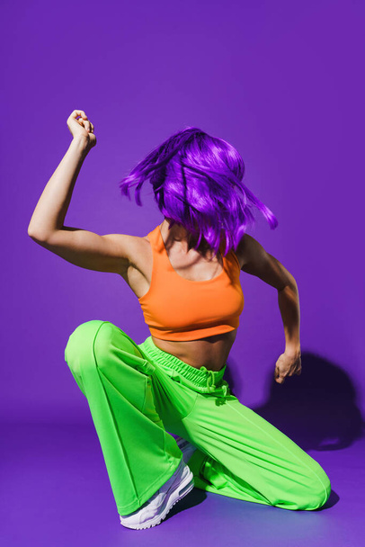Carefree active woman dancer wearing colorful sportswear performing against purple background - Foto, Imagem