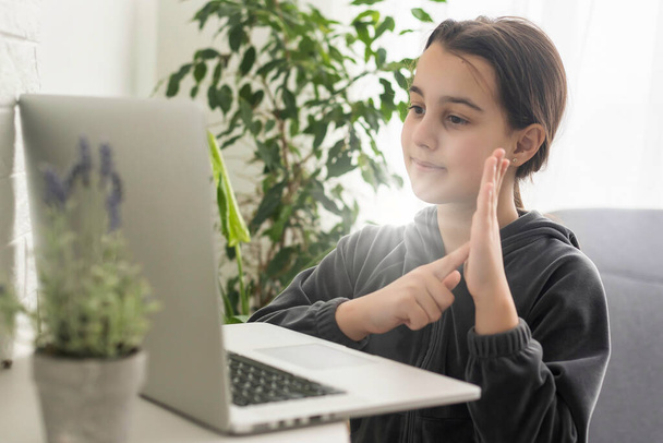 Uśmiechnięta nastolatka głucha niepełnosprawna uczennica szkoły online ucząca się na laptopie komunikująca się z nauczycielem za pomocą wideokonferencji telefonicznej używając języka migowego pokazującego gest dłoni podczas wirtualnej lekcji - Zdjęcie, obraz