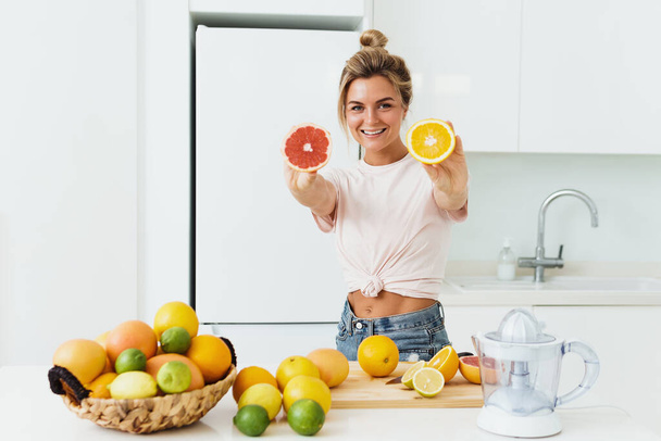 Young cheerful woman with a lot of citrus fruits during fresh juice preparation at home - Foto, imagen