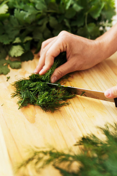 Closeup of female hands with knife chopping dill on wooden cutting board - Foto, immagini