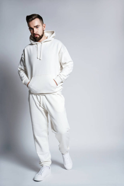 Handsome man wearing blank white hoodie and pants posing on gray background - 写真・画像