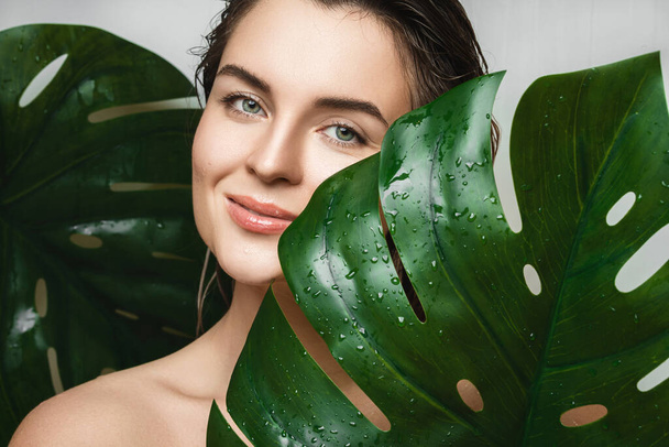 Portrait of beautiful young woman with a smooth skin holding Monstera deliciosa plant leaf - Foto, Imagen