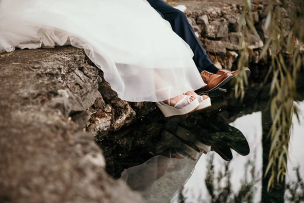 The legs of groom and bridge sitting at the shore of a pond - Foto, imagen