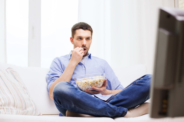 man watching tv and eating popcorn at home - 写真・画像