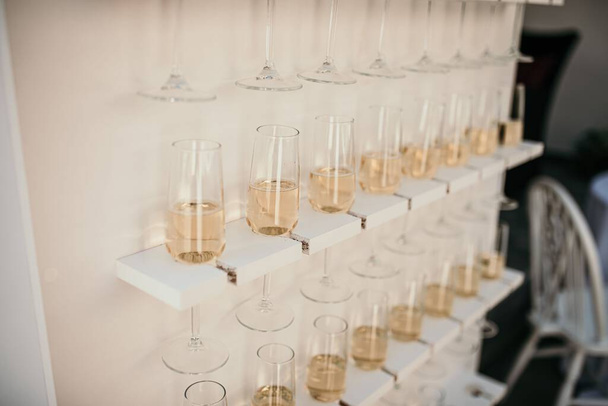 A bunch of glasses full of champagne hanging from the wall on the blurred background - Foto, Bild