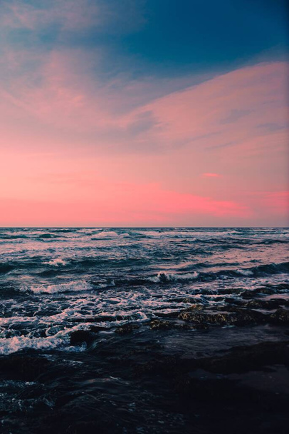 A vertical shot of a seascape under pink and blue clouds in the sky - Photo, image