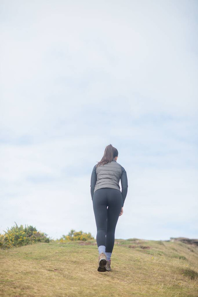A back view of a female walking on a hill against cloudy sky - Фото, изображение