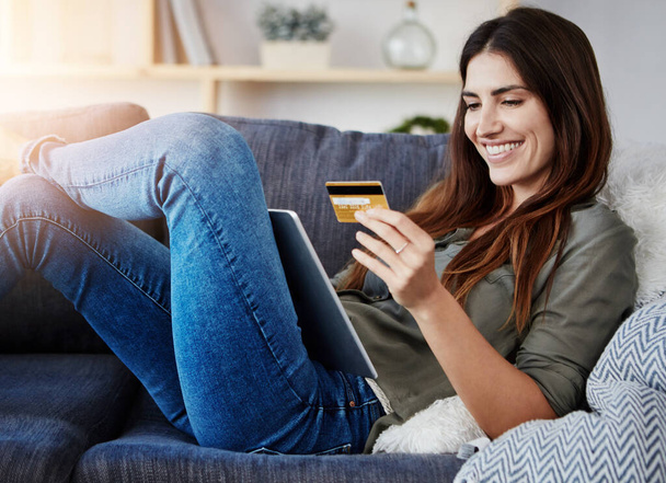 I love how easy it is to get what I need. a young doing online shopping while relaxing on her couch at home - Foto, Imagen
