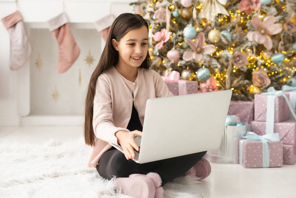 A girl during Christmas, sitting at home in the kitchen, congratulates her friends or grandparents via video communication. - Фото, изображение