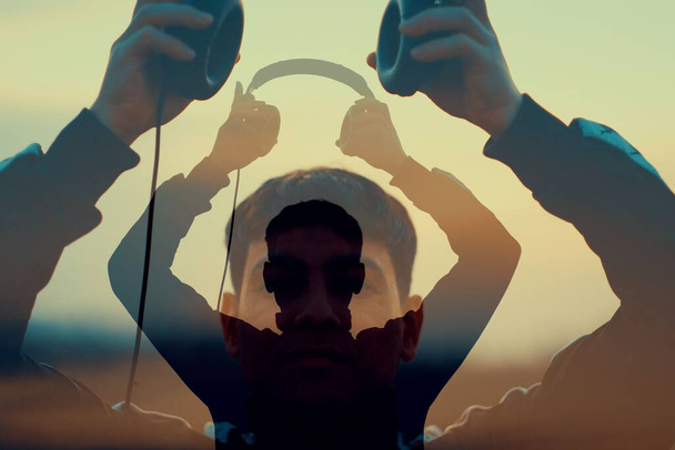 The silhouette of a young man putting on the headphones with his projections at sunset - Zdjęcie, obraz