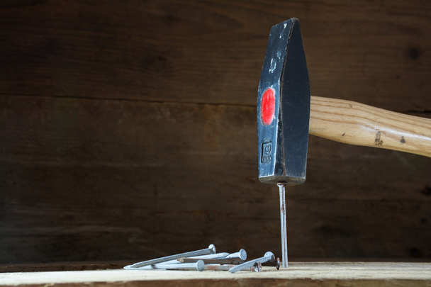 Hammer schlägt auf einen Nagel, dunkler Holzhintergrund mit Copyspace - Foto, Bild