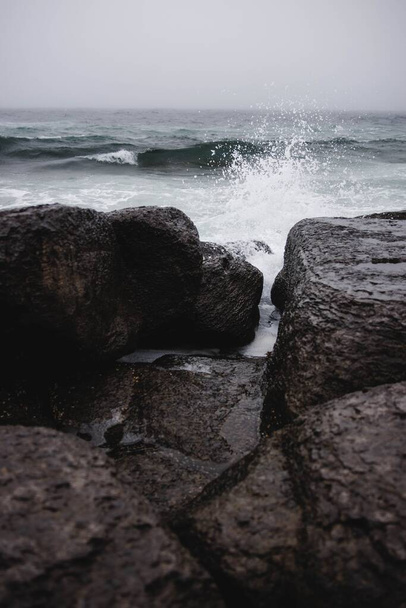 A vertical shot of water crashing on rocks in Newfoundland - Zdjęcie, obraz