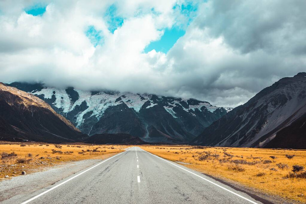 An asphalt road leading to a mountainous landscape under a blue sky - Foto, Bild