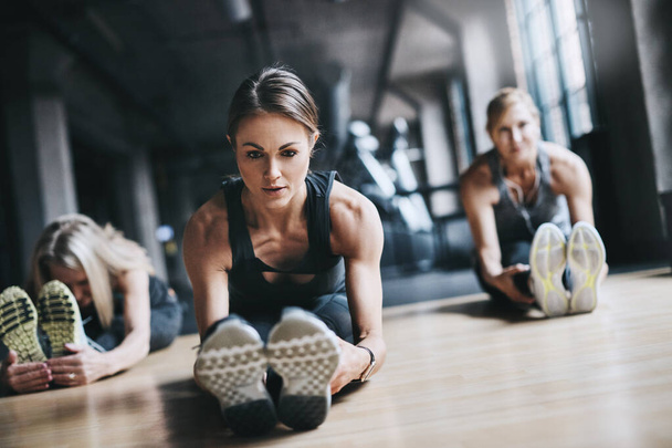 Preparare i muscoli. Colpo completo di tre donne attraenti e atletiche che si allungano prima del loro allenamento in palestra - Foto, immagini