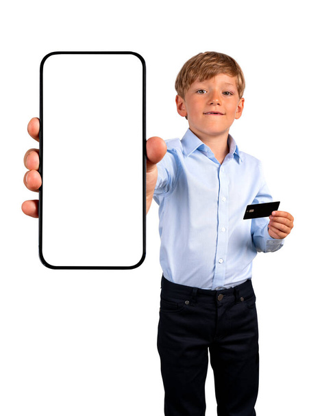 Child boy showing a smartphone with copy space mock up screen, holding a credit card. Isolated over white background. Concept of online payment, shopping and mobile app - Foto, imagen