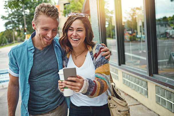Voy a la radio el fin de semana. una feliz pareja joven usando un teléfono inteligente mientras pasan el día en el centro de la ciudad - Foto, Imagen
