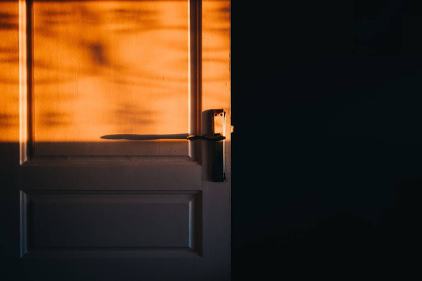 A vintage door under the golden sunlight shining through the window in the dark and empty room - Foto, Imagen