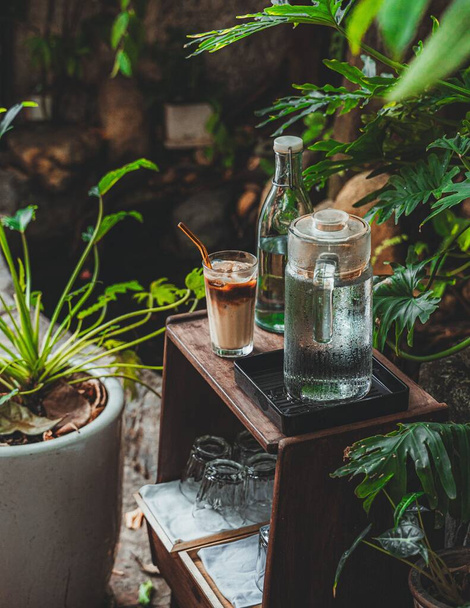A vertical shot of a wooden cafe table with jugs of water and an iced latte in a cafe - Fotoğraf, Görsel