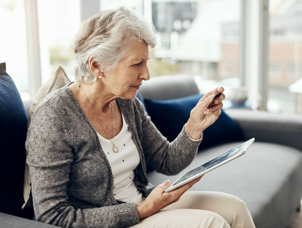 Seguendo i semplici passi per il checkout. una donna anziana in possesso della carta di credito durante la navigazione su un tablet digitale - Foto, immagini