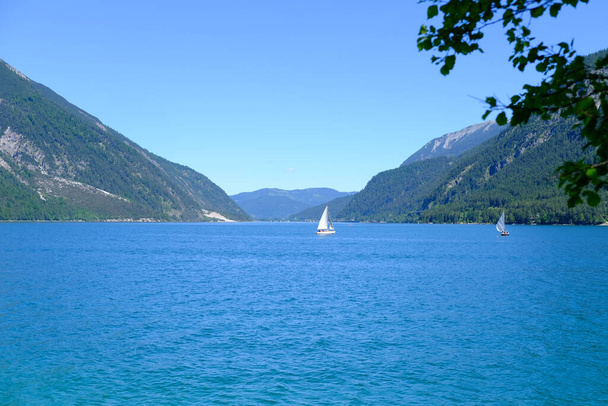 beautiful yacht floats under white sail on picturesque lake Achensee in Austria, green mountains rises above calm expanse of water, concept of vacation by reservoir, water sports, resort place tyrol - Valokuva, kuva