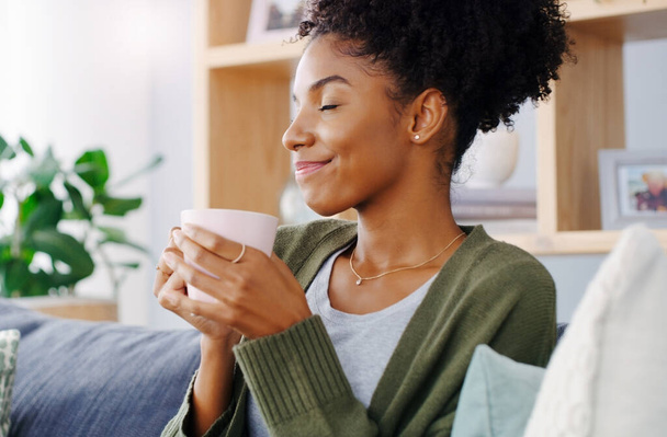 Hmm, ez a legjobb kávé a világon. egy vonzó fiatal nő kezében egy kávésbögre, miközben ül a kanapén a nappalijában - Fotó, kép
