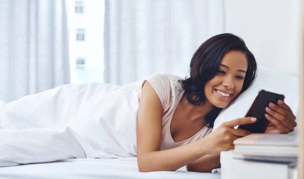 Eerste browsersessie van de dag. een jonge vrouw wakker in de ochtend en met behulp van haar telefoon in bed - Foto, afbeelding