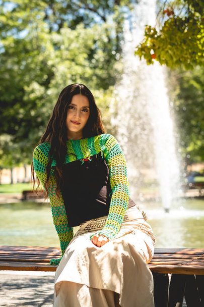 Enchanting latina charm: beautiful brunette model with a green knitted sweater in a sunny day in the park - Foto, Bild