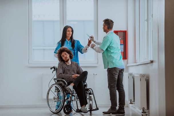 Doktor ve hemşire hastaların sağlığını tartışırken tekerlekli sandalyedeki hasta onların yanında. - Fotoğraf, Görsel