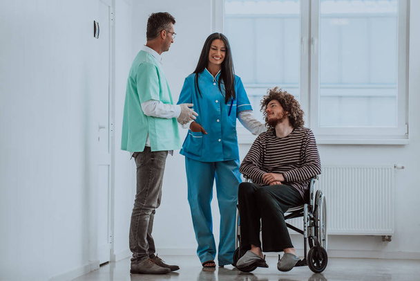 Врач и медсестра обсуждают здоровье пациентов, пока пациент в инвалидном кресле находится рядом с ними - Фото, изображение