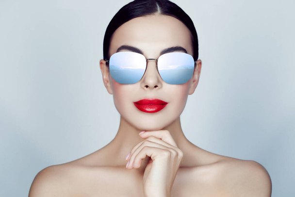 Attractive woman in stylish sunglasses on light grey background. Sky with clouds reflecting in lenses - 写真・画像