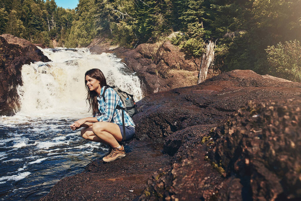 Doğadan bir not, akışına bırak. Çekici genç bir kadın kayalık bir nehir ve şelalenin yanında çömeliyor. - Fotoğraf, Görsel