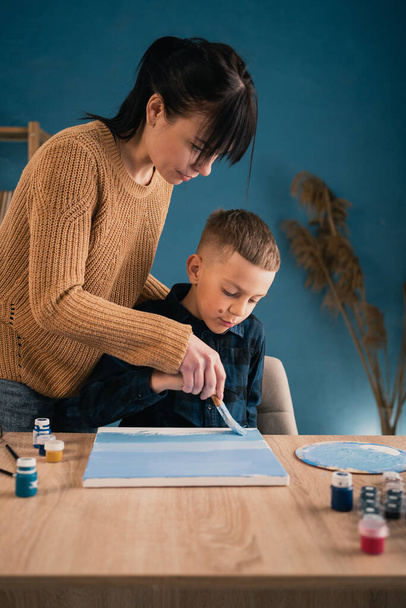 Mamma aiuta suo figlio uno scolaro a dipingere un quadro con vernici su tela. Hobby e tempo libero condivisi. copia spazio - Foto, immagini
