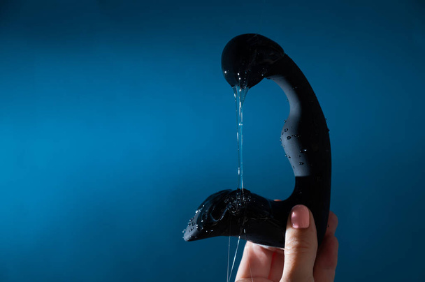 A woman pours lubricant on a black prostate stimulator on a blue background. Mens health prevention concept - Valokuva, kuva