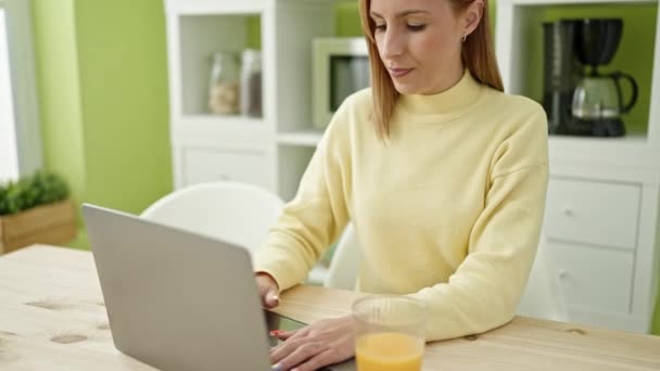 Young blonde woman using laptop having breakfast at home - Felvétel, videó
