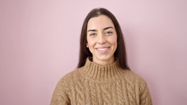 Νεαρή όμορφη ισπανόφωνη γυναίκα χαμογελά με αυτοπεποίθηση στέκεται πάνω από απομονωμένο ροζ φόντο - Πλάνα, βίντεο