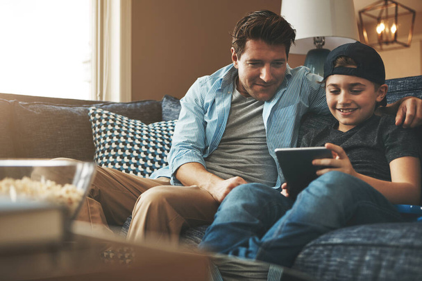 Uso seguro de Internet con la supervisión de los padres. un padre y su hijo usando una tableta digital juntos en el sofá en casa - Foto, imagen