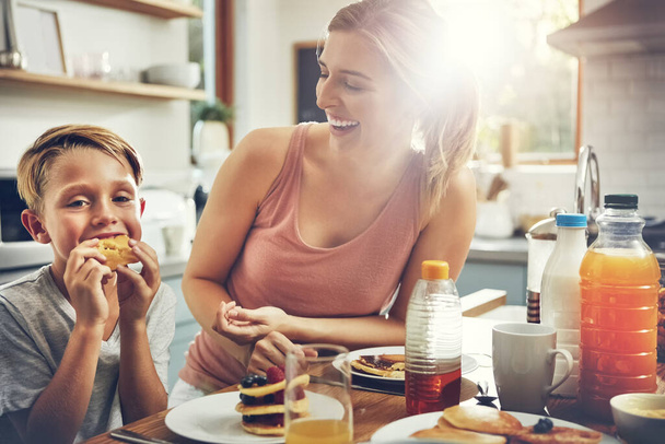 パンケーキがお気に入りです。朝食を食べながら息子と座っている女性が - 写真・画像