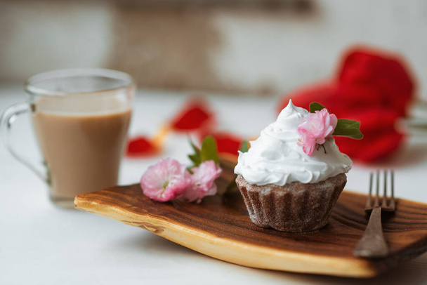 Τούρτα και καφές. Νόστιμο κέικ με κρέμα και ροζ διακόσμηση λουλουδιών σε ξύλινο πιάτο. Κόκκινα λουλούδια στο φόντο. Καλημερα. Τέλειο πρωινό. - Φωτογραφία, εικόνα