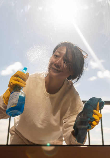 Крупним планом азіатська жінка Руки Очищення вікна за допомогою обприскувача рідини
. - Фото, зображення